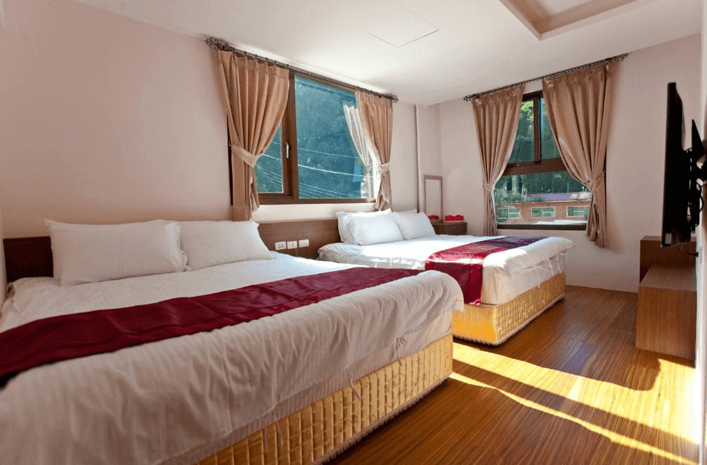 【溪頭住宿】溪頭新景宏渡假村民宿的房間內設有兩張大床，搭配柔和的燈光與暖色系窗簾，明亮的窗戶提供充足的自然光線，讓空間更加溫暖且舒適，適合家庭或朋友入住。