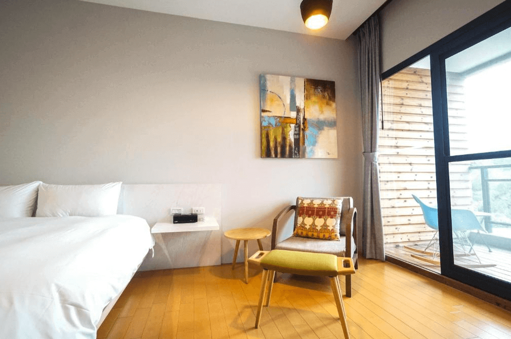 【溪頭住宿】溪頭有晴天民宿的房內配置溫暖的木地板與精緻的裝飾畫，搭配舒適的單椅與陽台空間，讓旅客能在清晨或傍晚時光欣賞戶外景致，享受悠閒時光。