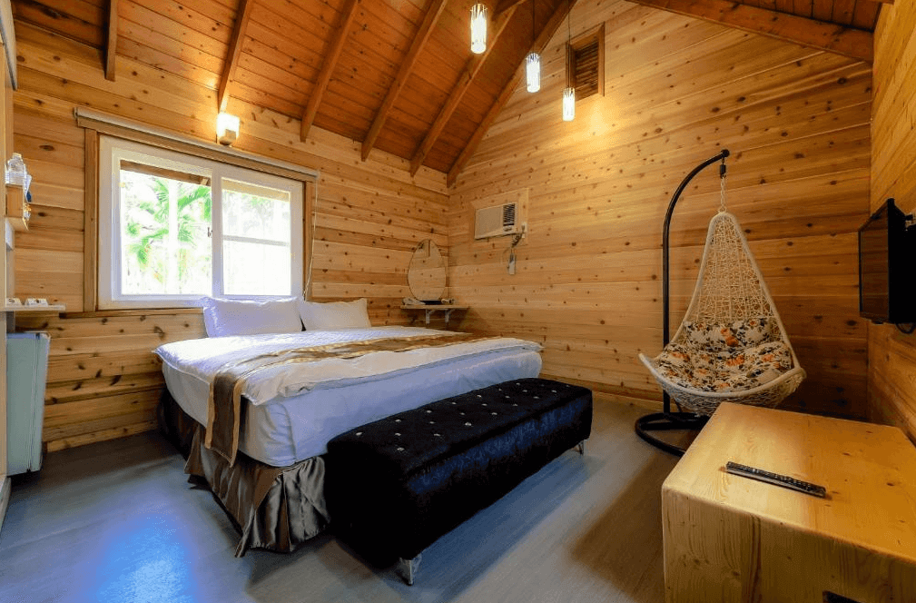 【溪頭住宿】溪頭杉溪鹿溜滑梯小木屋的房間以全木質設計為特色，散發出溫暖的自然氣息，搭配高挑的斜屋頂與柔和的燈光，營造出溫馨的住宿環境，還有一張舒適的吊椅，讓旅客享受放鬆時光。