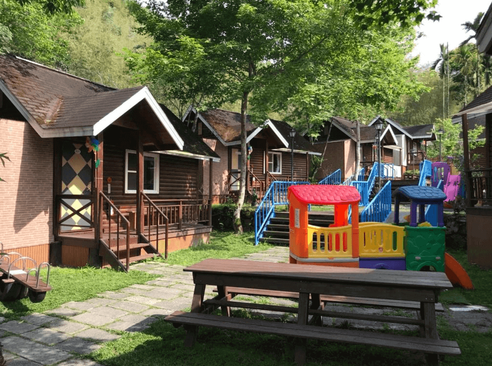 【溪頭住宿】溪頭杉溪鹿溜滑梯小木屋的外部環境為童話風格的小木屋群，庭院內設有木製座椅與小型遊樂設施，四周綠意盎然，是親子旅行或團體旅遊放鬆心靈的理想選擇。