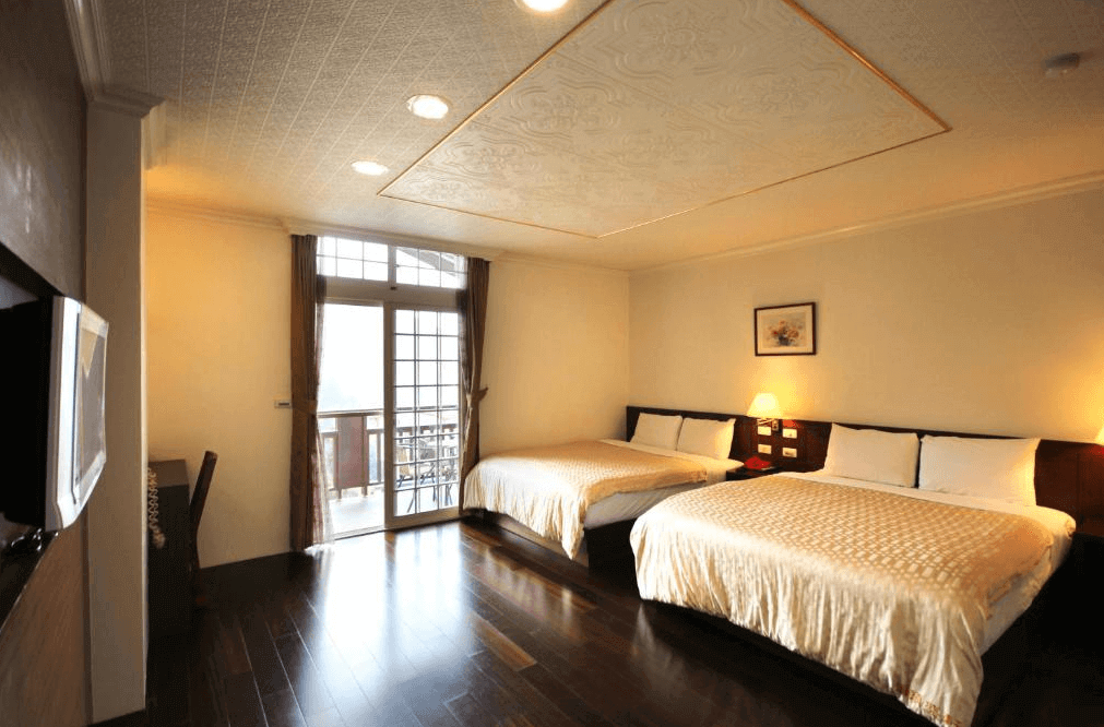【溪頭住宿】溪頭盛軒森林會館的房間內設有兩張大床，搭配深色木地板與簡約的燈光設計，明亮的窗戶連接小陽台，提供旅客俯瞰外部自然景致的機會，空間感溫暖且舒適。