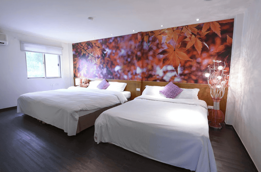 【烏來住宿】烏來名湯溫泉會館的房間內設有兩張雙人床，床頭背景牆採用秋葉圖案，營造溫暖自然的氛圍。房間採光良好，簡約的白色牆面搭配現代燈飾，整體感覺舒適而溫馨。