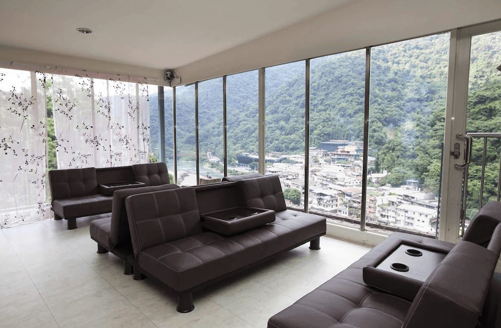 【烏來住宿】烏來名湯溫泉會館的觀景休息區配有深棕色沙發與透明落地窗，窗外可欣賞山城景色與自然美景。空間明亮寬敞，適合休息或與朋友聊天，設計簡約而不失雅致。