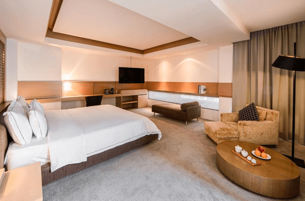 【烏來住宿】璞石麗緻溫泉會館的房間內配置柔軟的大床與舒適的沙發座椅，搭配溫暖的燈光與米色窗簾。空間寬敞，提供小茶几和果盤，整體設計典雅且放鬆，非常適合靜享時光。