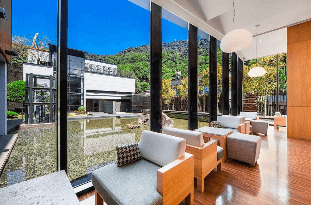 【烏來住宿】璞石麗緻溫泉會館的公共休憩區以大片落地玻璃環繞，提供開闊的視野與自然採光。窗外可見水景與綠意景致，搭配木質家具與柔和的燈光，空間氛圍雅致且愜意。