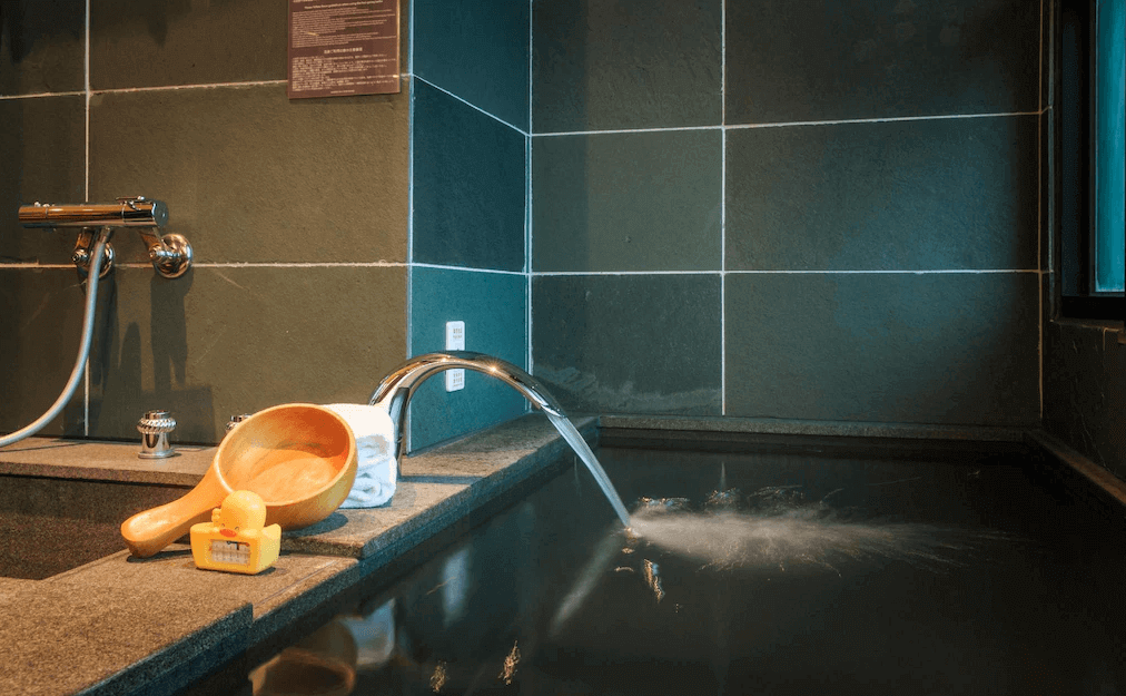 【礁溪住宿】礁溪福朋喜來登酒店的私人泡湯池，使用深色石材打造，水龍頭正在注水，池邊放置木製舀水勺與玩具鴨，營造舒適且放鬆的泡湯氛圍。