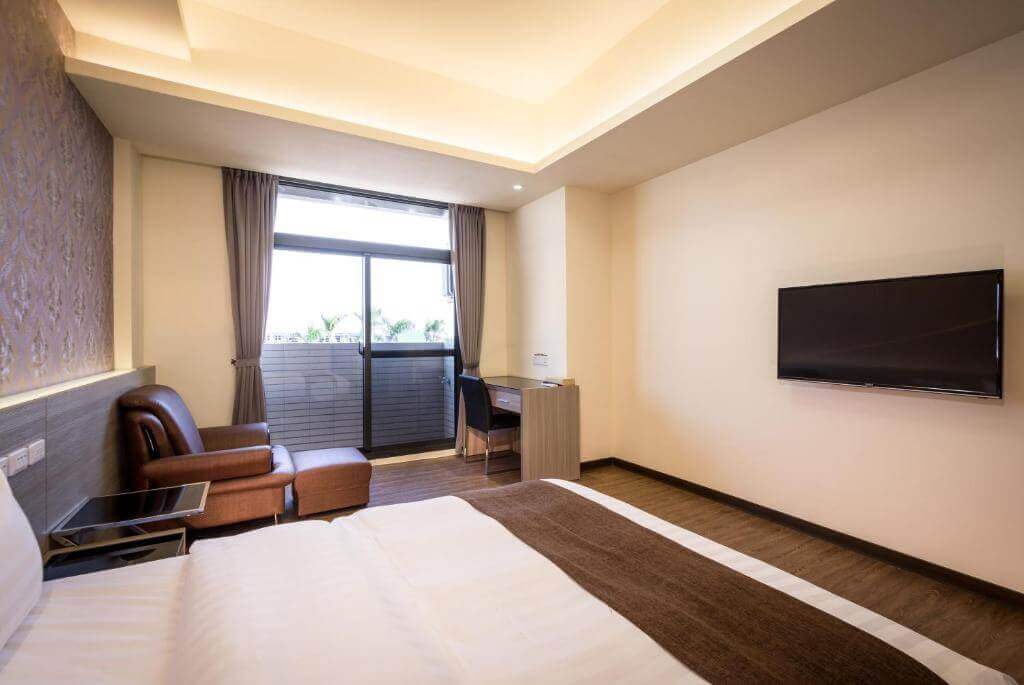 【北港住宿】禾都商務飯店的房內設有工作桌與電視，窗戶帶有自然採光，淺棕色窗簾搭配柔和的室內色調，空間感十足，適合商務或旅遊休憩。