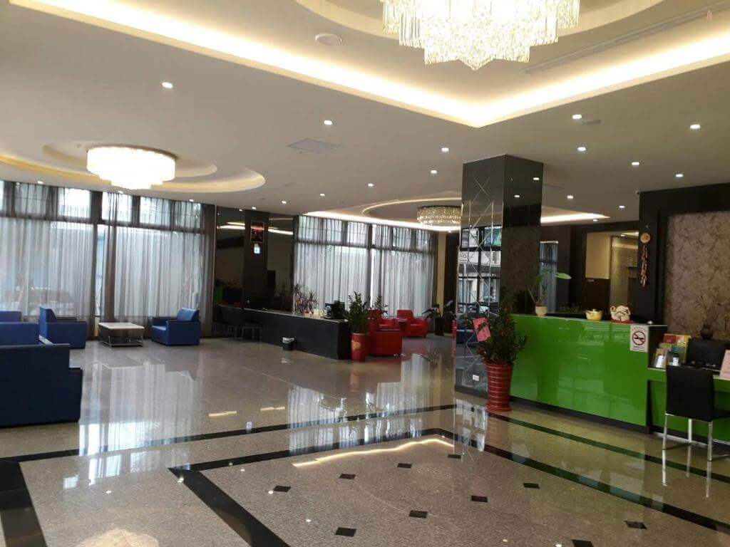 【北港住宿】禾都商務飯店的大廳寬敞明亮，吊燈華麗，藍色與紅色沙發分區擺放，綠色櫃檯增添一抹活力，展現現代化的設計風格與舒適氛圍。