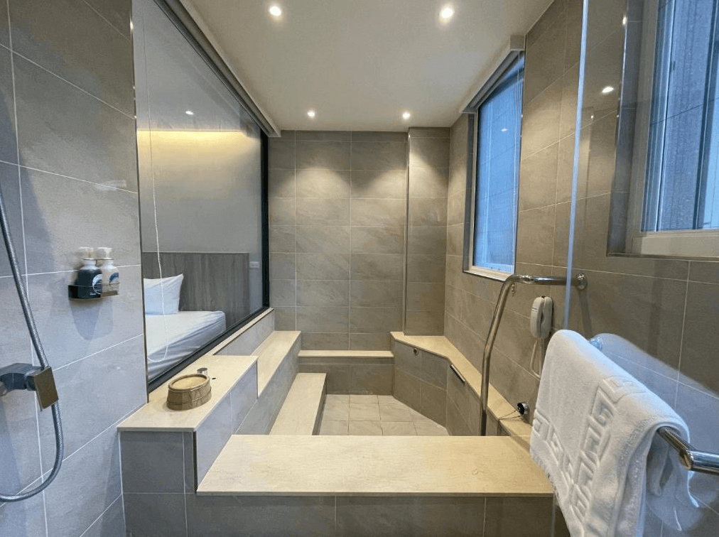 【烏來住宿】足立司拉 SLA ULAY的浴室，鋪設淺色瓷磚，具備寬敞的淋浴區及座椅設計。浴室與臥室之間採用透明玻璃，配有窗戶讓自然光透入，空間感十足。