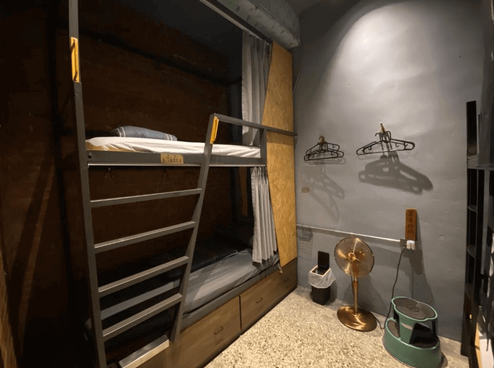 【玉里住宿】途中玉里青年旅舍雙層床的房間，牆上掛有簡單的衣架和一個復古風扇，空間設計注重實用性且兼具工業風格。