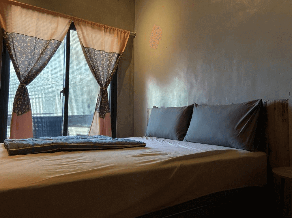 【玉里住宿】途中玉里青年旅舍的雙人房，房內有一張大床，床頭兩側搭配簡單的床頭櫃，窗戶掛著碎花窗簾，營造出溫馨的氛圍。