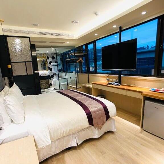 【大湖住宿】采莓行館Caimei Hotel的雙人房，配有寬敞的窗戶與都市景觀。房間內有舒適的雙人床，搭配淺色木質地板與簡約的工作桌，並配有大型掛牆電視，整體設計明亮且具時尚感。