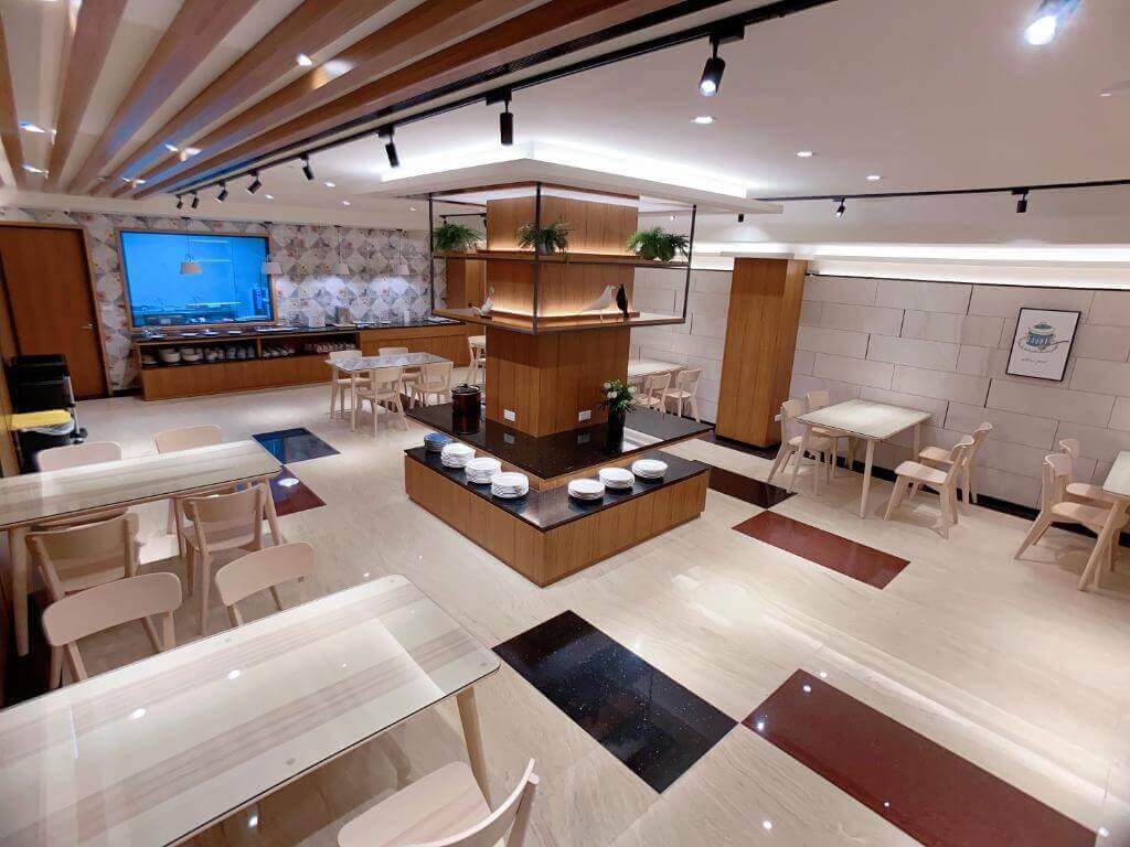 【大湖住宿】采莓行館Caimei Hotel的用餐區，採用溫暖的木質與明亮的燈光設計，擺放了多張簡約風格的餐桌椅。中央有一個帶綠植的展示櫃，整體空間寬敞且清新，適合家庭或團體聚餐。