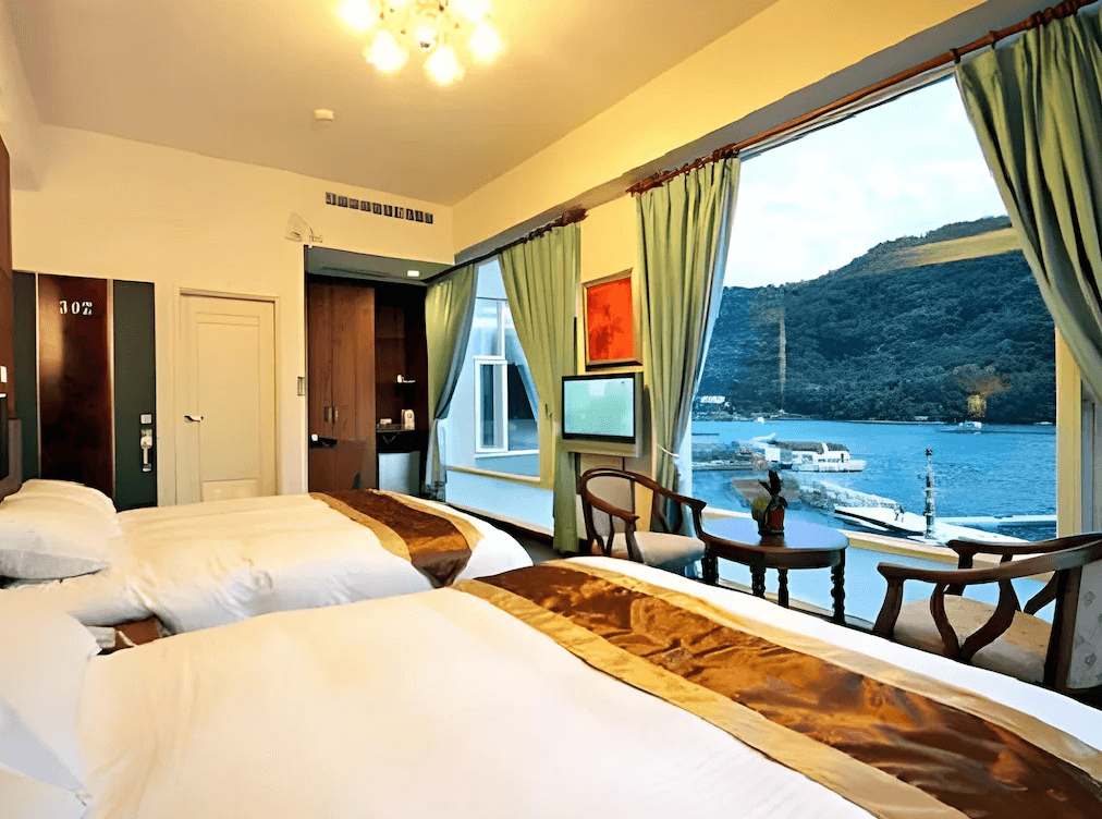 【日月潭住宿】H& 日月潭水漾的房內兩張雙人床對著窗邊擺放，窗外景色秀麗，設計以暖色調為主，搭配窗簾增添隱私感，房間布置溫馨且實用。