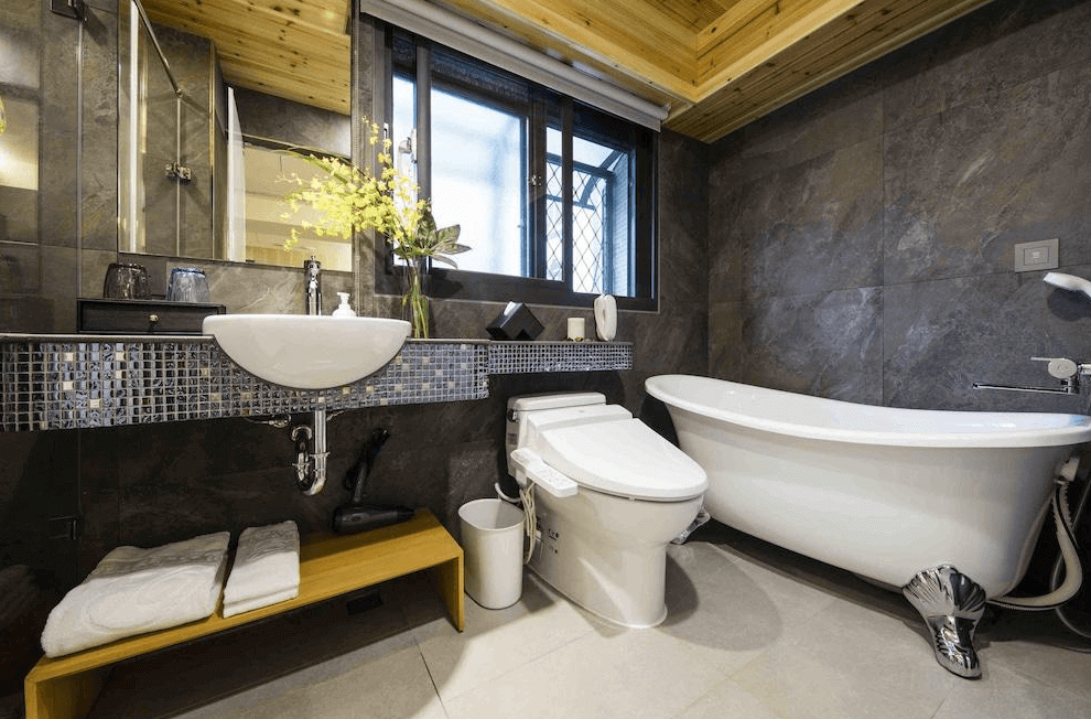 【寧夏夜市住宿】Hotel I Journey 愛行旅的白色浴缸、洗手台和高級馬桶，牆面為深灰色大理石材質，搭配木質天花板，展現現代與自然的結合。