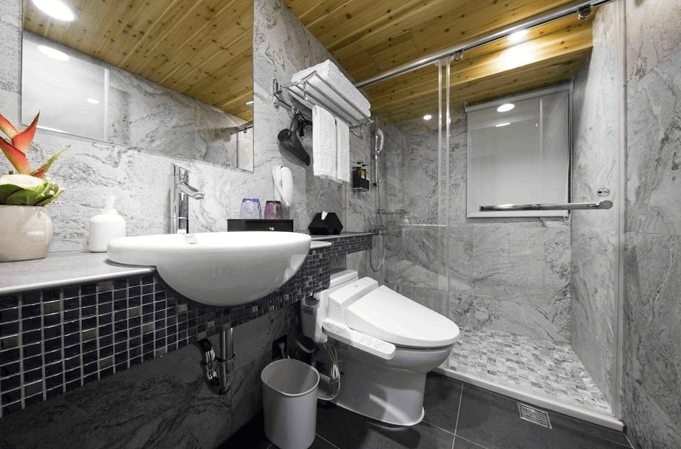 【寧夏夜市住宿】Hotel I Journey 愛行旅的浴室，採用大理石牆面與木質天花板，配備玻璃淋浴間、洗手台和高級馬桶，整體設計簡潔且實用。