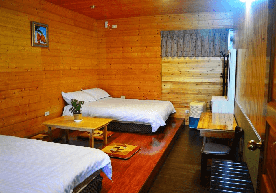 【阿里山住宿】仲明居陶藝坊的房間內部以木質裝潢為主，搭配兩張舒適的床鋪，呈現溫暖的鄉村風格。中央的小茶几和座墊營造出一個放鬆的休憩空間，適合家庭或好友入住。