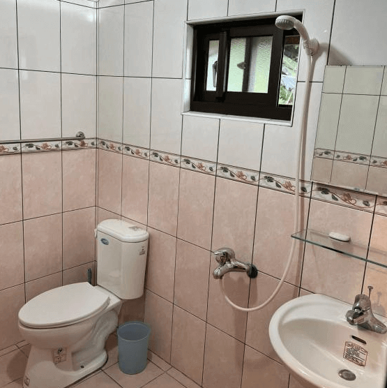 【阿里山住宿】仲明居陶藝坊的浴室以淺粉色與白色瓷磚為主，搭配基本的洗手台、馬桶與淋浴設備。設計簡約，整潔且實用，滿足住客的基本需求。