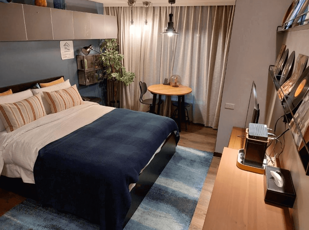 【寧夏夜市住宿】優美飯店的房間內裝飾現代且溫馨，深藍色的床單搭配多彩靠墊，木質地板與窗簾營造出居家的氛圍，房內設有圓桌和兩張高腳椅，適合小型聚會或用餐。