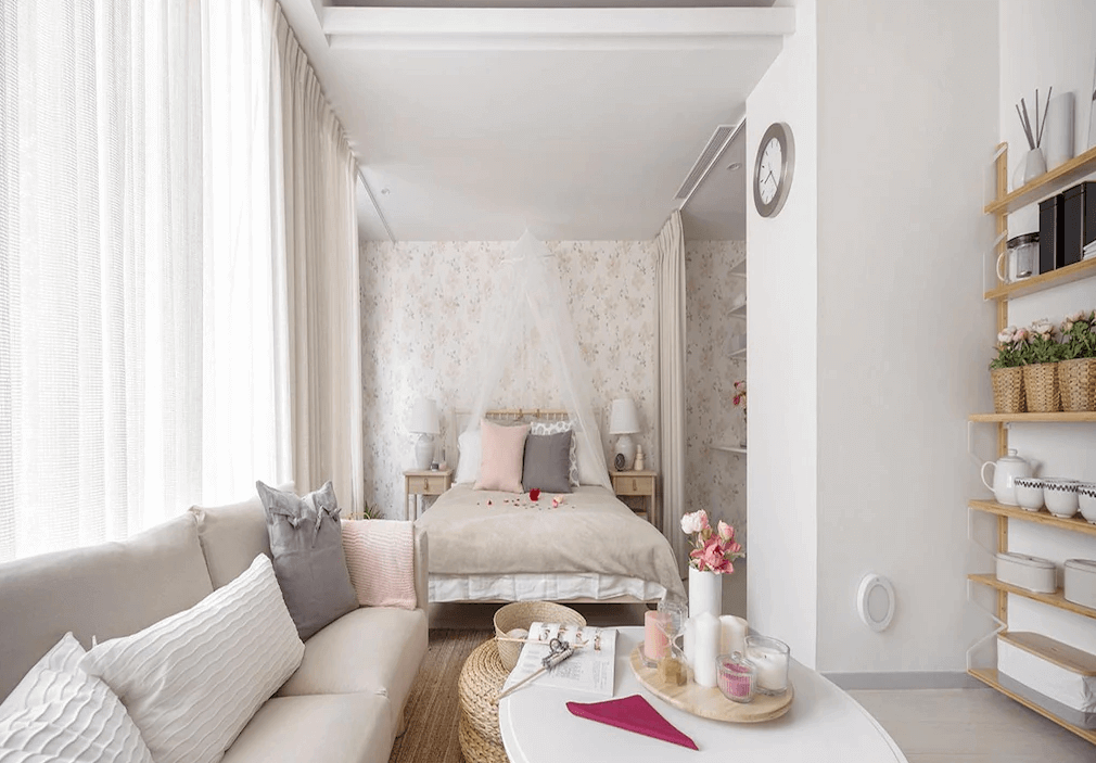 【寧夏夜市住宿】優美飯店的房間以柔和的粉色和米色為主題，白色的蚊帳增添了浪漫氣息，搭配沙發與木質裝飾架，擺放著簡約的家庭擺設。