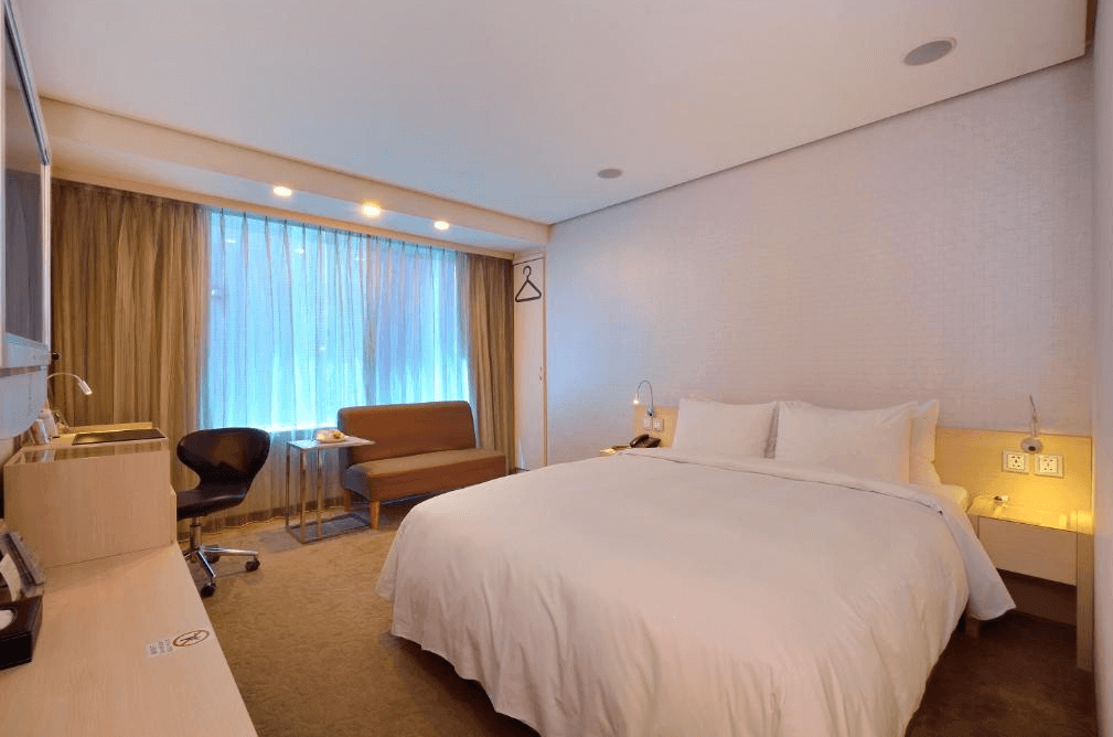 【寧夏夜市住宿】優美飯店的房間簡約明亮，白色的床單與淺色牆壁搭配，窗邊有一張棕色沙發和掛衣架，帶來舒適與實用性的結合。