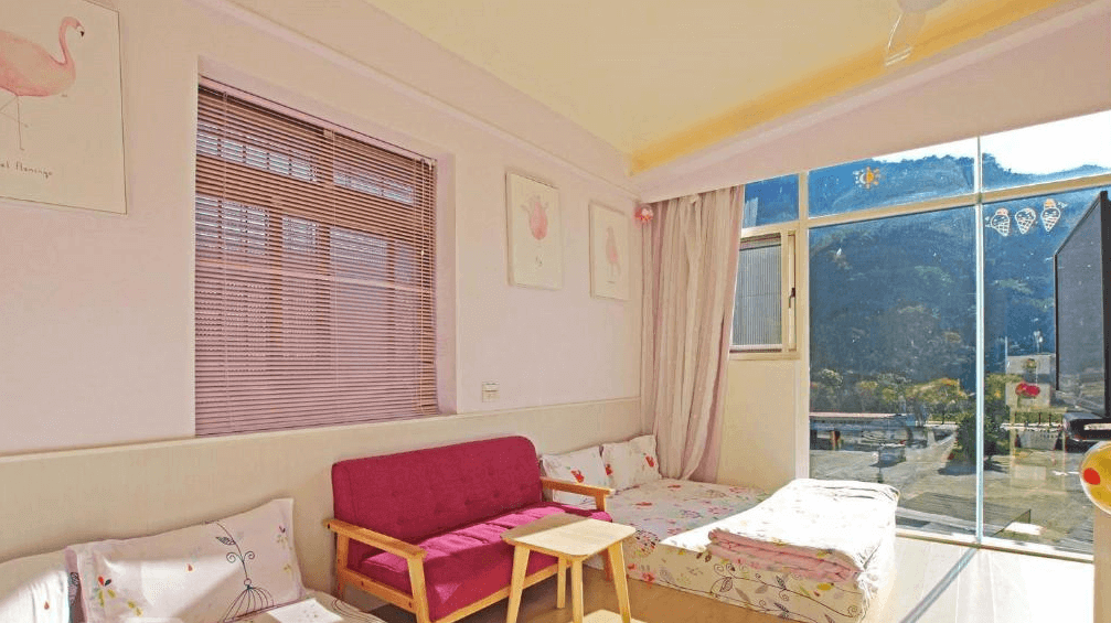 【司馬庫斯住宿】內灣-彎月民宿的明亮房間，窗外可欣賞山林景色，房內有多組地墊床鋪和粉色沙發，牆面掛有粉色主題的裝飾畫，空間溫馨舒適。