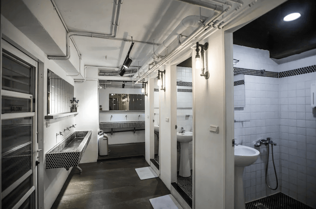 【台北車站住宿】【寧夏夜市住宿】"台北車站青年旅館"北門臥客青年旅舍的衛浴空間，內部以白色磁磚和黑白馬賽克為裝飾，設有多個洗手台和淋浴間，燈光柔和，整體乾淨有序。