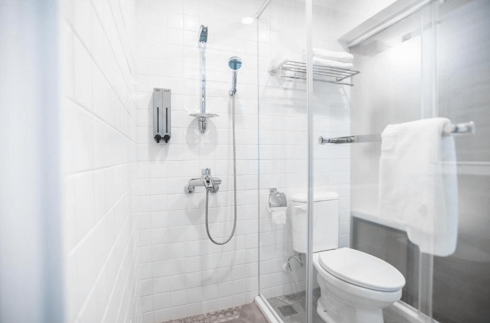 【台北車站住宿】【寧夏夜市住宿】"台北車站青年旅館"北門臥客青年旅舍的私人浴室，設有玻璃淋浴間、馬桶和白色牆磚，配備基本的洗浴設施，空間明亮整潔。