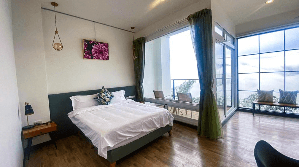 【阿里山住宿】十方山水明亮的雙人房內設有大床與座椅區，通往戶外陽台，窗外景致一覽無遺。室內以木地板與柔和的綠色窗簾增添溫馨氛圍，適合兩人悠閒入住。