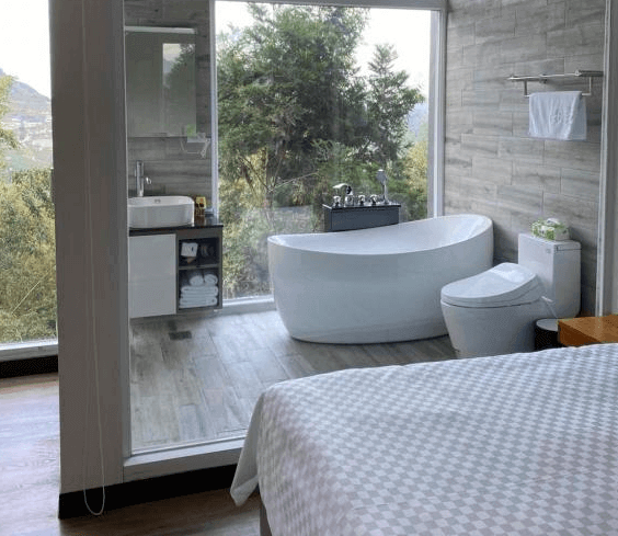 【阿里山住宿】十方山水的浴室內設有獨立浴缸與全景玻璃窗，讓住客在沐浴時亦能欣賞窗外的自然風光。浴室內採用木紋瓷磚，融合現代與自然元素，營造放鬆且雅緻的氛圍。