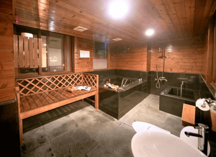 名廬假期大飯店現代日式風格的私人湯屋，以深色石材與木質元素打造沉穩低調的泡湯空間。房內設有兩座獨立溫泉浴池與木質長凳，提供寬敞舒適的泡湯體驗，柔和燈光與簡約設計讓人身心放鬆，享受純粹的溫泉療癒。