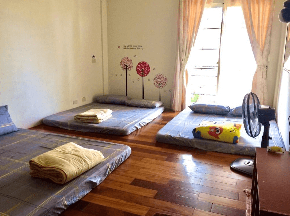 【嘉義寵物友善住宿】圓方居民宿適合多人入住的房間，地板為深色木質，擺放多張藍色床墊，牆面裝飾有卡通樹和文字圖案，窗戶設有柔和的米色窗簾，採光良好，氣氛輕鬆。