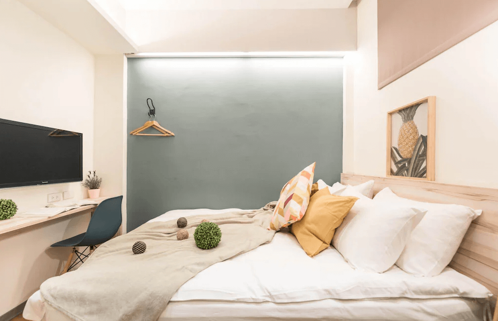 【寧夏夜市住宿】在家行旅-中山館的臥室，配有一張雙人床，靠牆擺放枕頭和裝飾抱枕，背景為綠灰色牆面，房內設有桌子和電視，營造溫馨且現代的住宿氛圍。