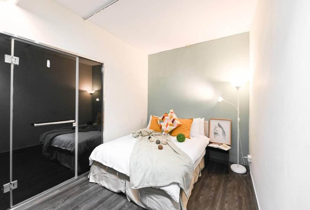 【寧夏夜市住宿】在家行旅-中山館的小型臥室，內部以綠灰色牆面為背景，配有一張雙人床，床上擺放多彩抱枕和裝飾毯，房間燈光柔和，地板為深色木質設計。