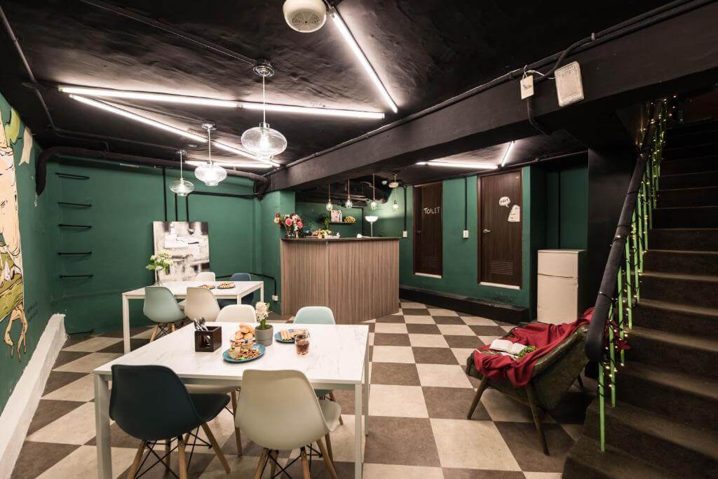 【寧夏夜市住宿】在家行旅-中山館的共用空間，設有綠色牆壁和黑色天花板，擺放多張白色桌椅，中央有一個櫃檯，裝飾著各種花卉，整體風格現代且富有設計感。