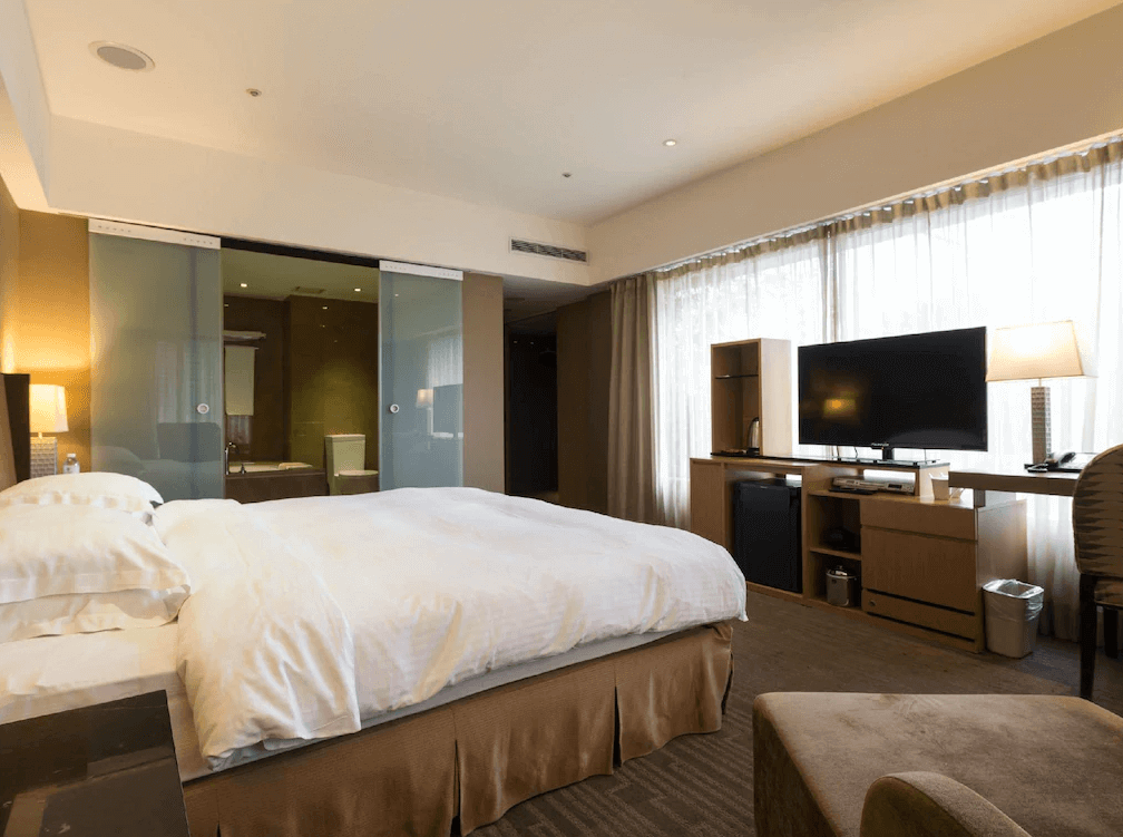 【寧夏夜市住宿】城市商旅-南西館的雙人房內部配有大床，玻璃隔間的浴室設計現代化，房內設有電視、迷你冰箱與書桌，窗簾後提供良好的採光，整體感覺明亮且高級。