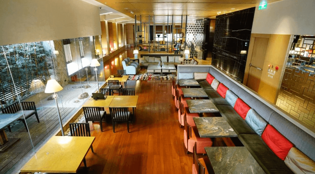 【寧夏夜市住宿】城市商旅-南西館的酒店大廳內部，設有多組餐桌與舒適的沙發區，玻璃牆提供自然採光，裝潢以木質地板與柔和燈光為主，空間寬敞且富有現代感。