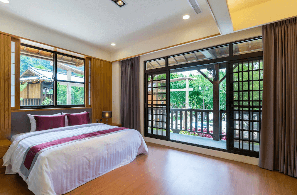 【埔里住宿】埔里夏都華蔓山林渡假會館的精緻雙人床房間，擁有落地窗及陽台設計，窗外可見花園美景，房間內裝潢以木質元素搭配暖色系燈光，營造溫馨舒適的氛圍。