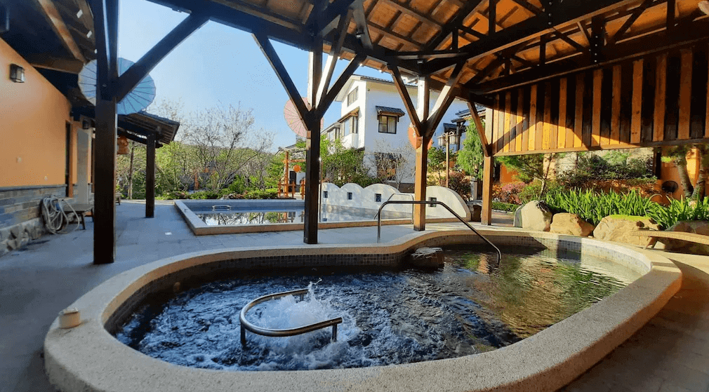 【埔里住宿】埔里夏都華蔓山林渡假會館的戶外溫泉設施，周圍被綠意盎然的花園環繞，木質結構的屋頂增添自然氛圍，適合在放鬆的環境中享受泡湯樂趣。