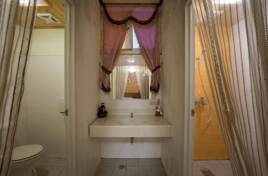 【埔里住宿】埔里小鎮歐式民宿與背包客棧的浴室採分離式設計，洗手台設置在中間，旁邊分別為馬桶與淋浴間。牆面以白色為主，搭配柔和的布簾裝飾，展現簡約而不失溫馨的風格。