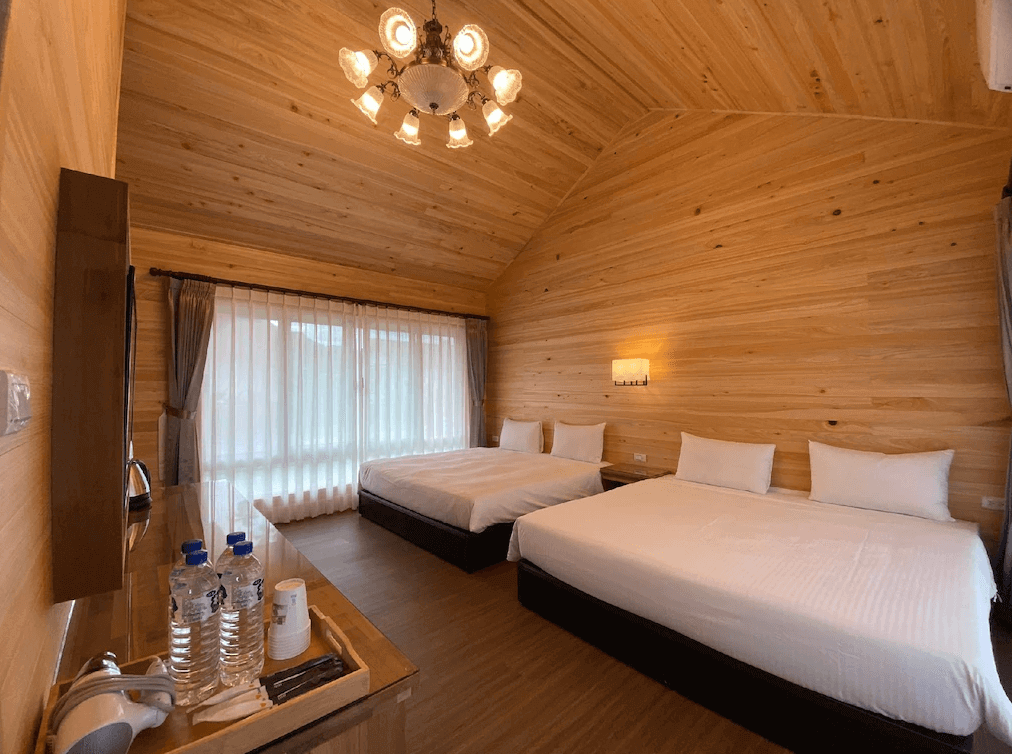 【埔里住宿】埔里日記木質裝潢為主的雙床房，整體採用溫暖的原木色調，天花板設有吊燈增添鄉村風情。房間內部乾淨明亮，窗戶帶有紗簾，提供柔和的自然光。