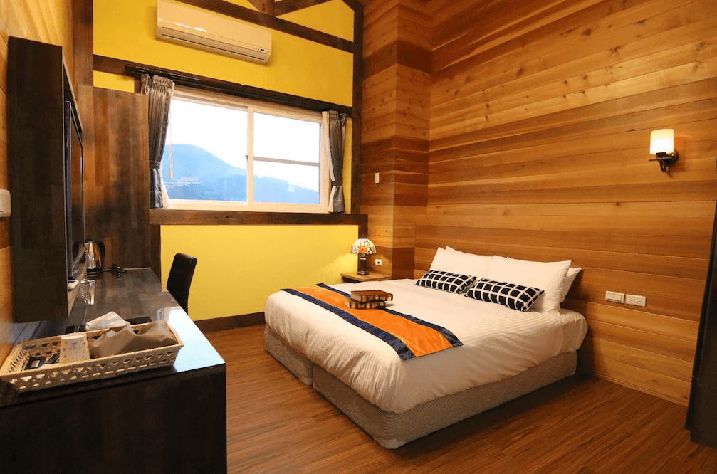 【埔里住宿】埔里日記的雙人房，牆面以木板搭配黃色點綴，營造溫暖氣氛。床上放置簡約的枕頭與橙色飾品，房間還設有書桌和窗戶，可欣賞外部景觀。
