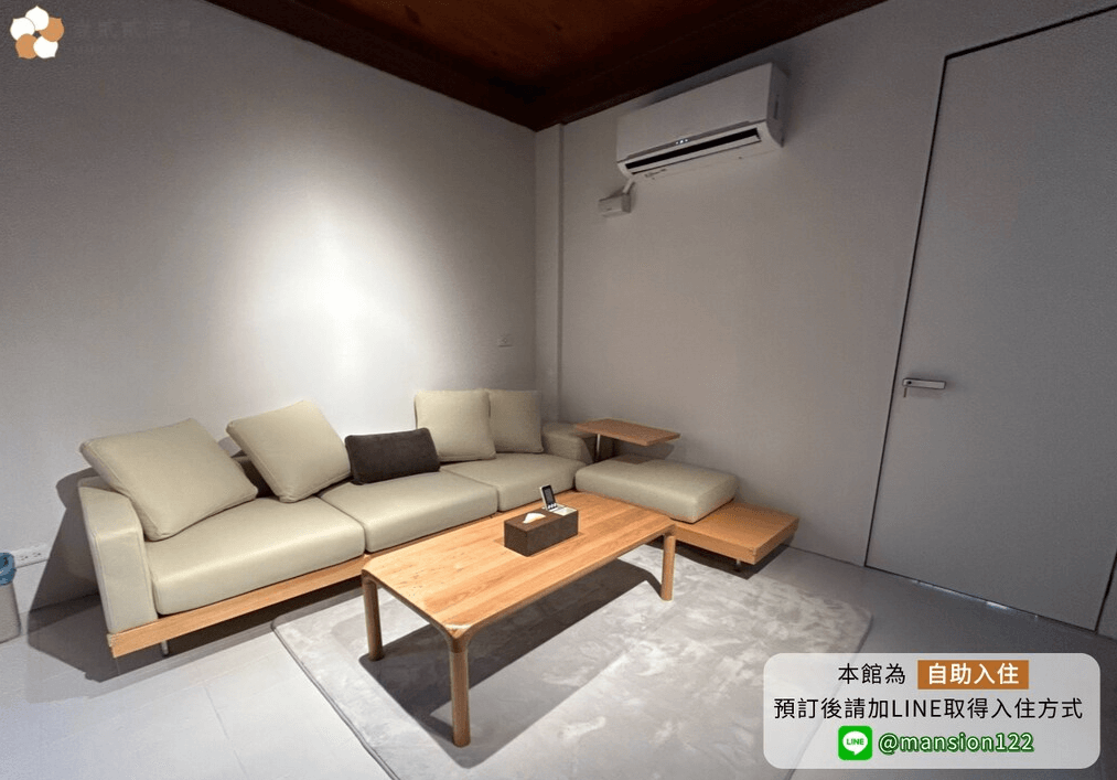 【嘉義寵物友善住宿】壹貳貳洋樓的客廳，設有米色L型沙發和木質茶几，房間採用簡約設計，牆面為白色，天花板為原木色調，搭配空調設備。