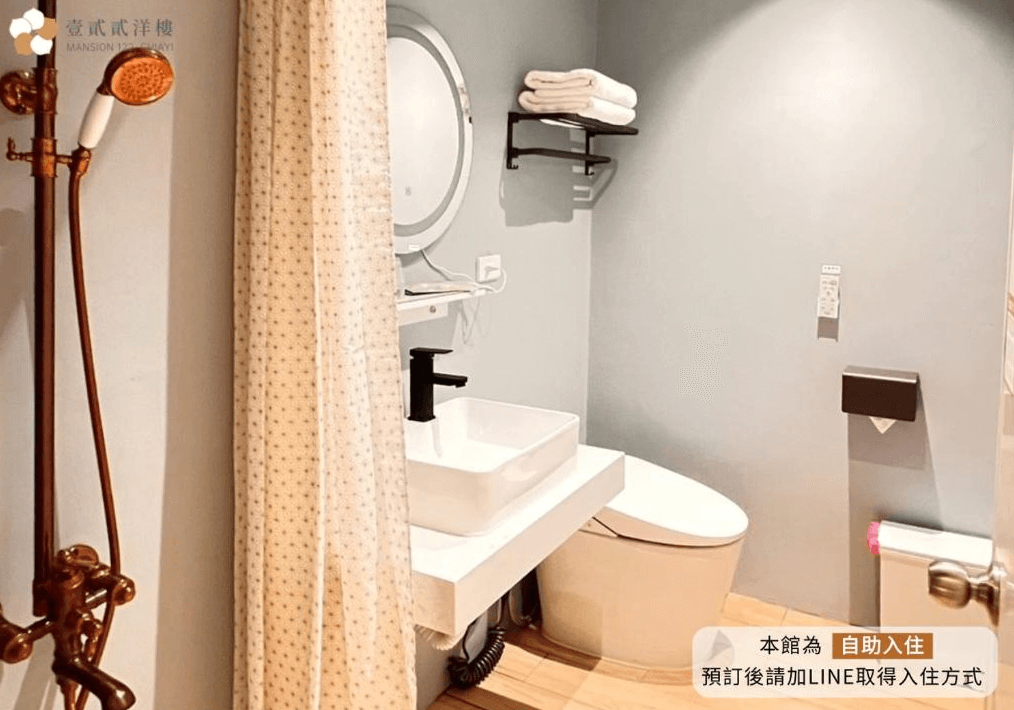 【嘉義寵物友善住宿】壹貳貳洋樓的衛浴空間，配有現代化設備，包括白色洗手台、圓形化妝鏡，以及帶花灑的古銅色淋浴設備，整體色調為淺灰色，設計簡潔清爽。