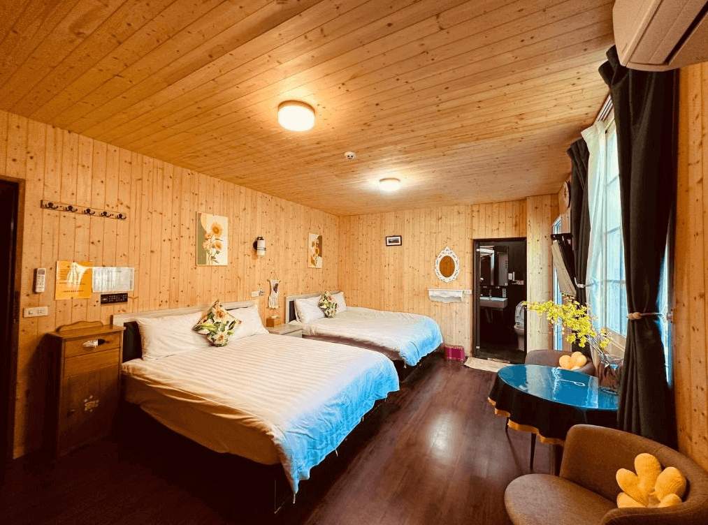 【阿里山住宿】大方茶業民宿的雙人床配置木質客房，寬敞明亮。牆上掛有精緻的裝飾畫，窗戶旁的小圓桌與椅子營造出一個適合放鬆或用餐的角落，十分溫馨。