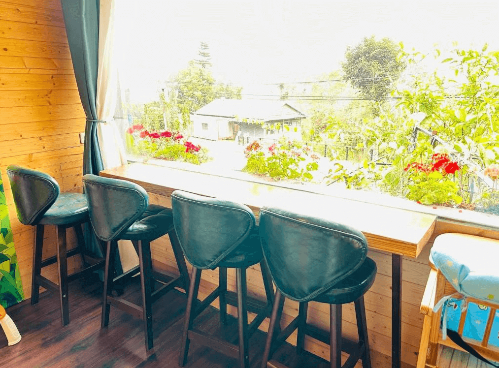 【阿里山住宿】大方茶業民宿的木質吧台搭配高腳椅，設置於窗邊，外景充滿綠意與花卉點綴，提供一個放鬆喝茶或閱讀的愜意空間。