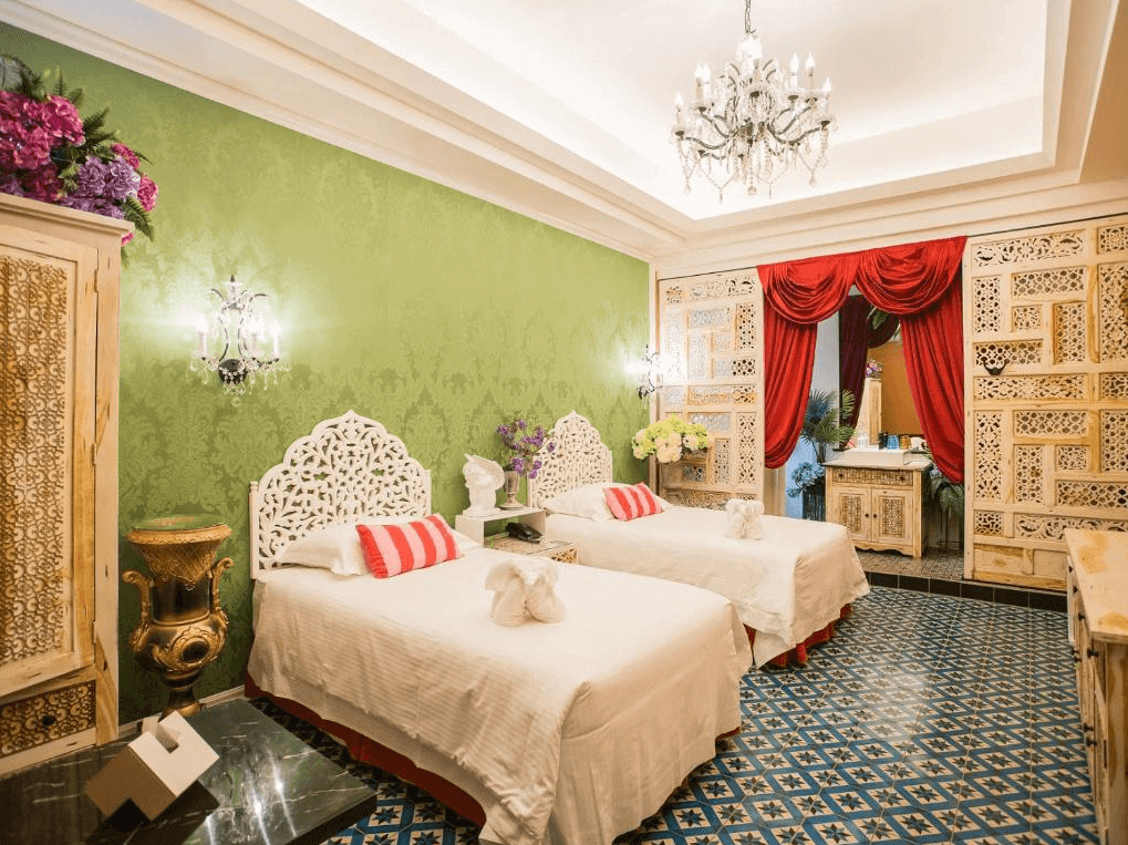 【嘉義寵物友善住宿】安娜國王酒店異國風情為主題的豪華客房，牆面為綠色搭配浮雕圖案，配有兩張白色床鋪和精緻的雕花床頭板，室內裝飾華麗，有吊燈和紅色窗簾，地面鋪設藍色花紋瓷磚。