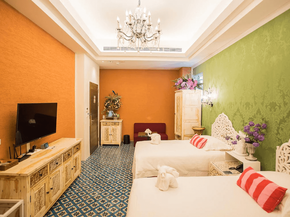 【嘉義寵物友善住宿】安娜國王酒店異國風情的客房內景，牆面橘綠色對比鮮明，配有吊燈、雕花木製家具和藍色花紋瓷磚地面，角落擺放裝飾性花藝，整體設計融合了豪華與溫馨。