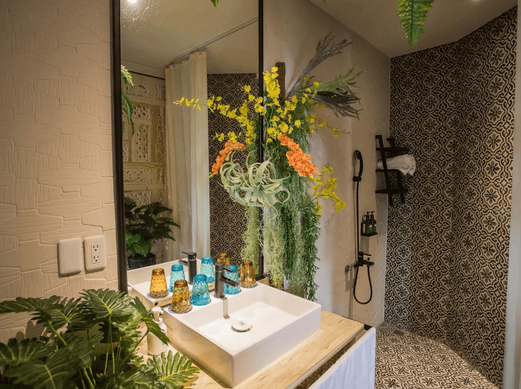 【嘉義寵物友善住宿】安娜國王酒店的浴室，配有大型化妝鏡和簡約白色洗手台，台面上擺放彩色玻璃杯，周圍以植物和鮮花點綴，牆面和地面採用復古花磚，淋浴區設備齊全。