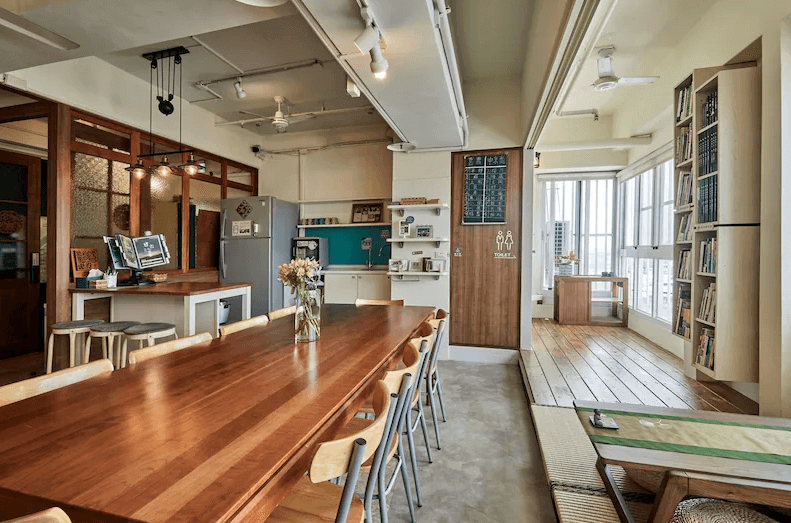 【嘉義寵物友善住宿】安蘭居旅店的公共空間，設有長木桌和多張椅子，內部有開放式廚房與書架，裝飾簡約且功能性強，適合團體活動或聚會。